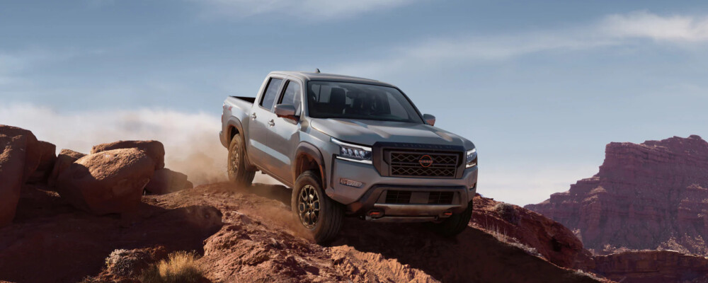 A silver 2022 Nissan Frontier drives down a rocky hill.