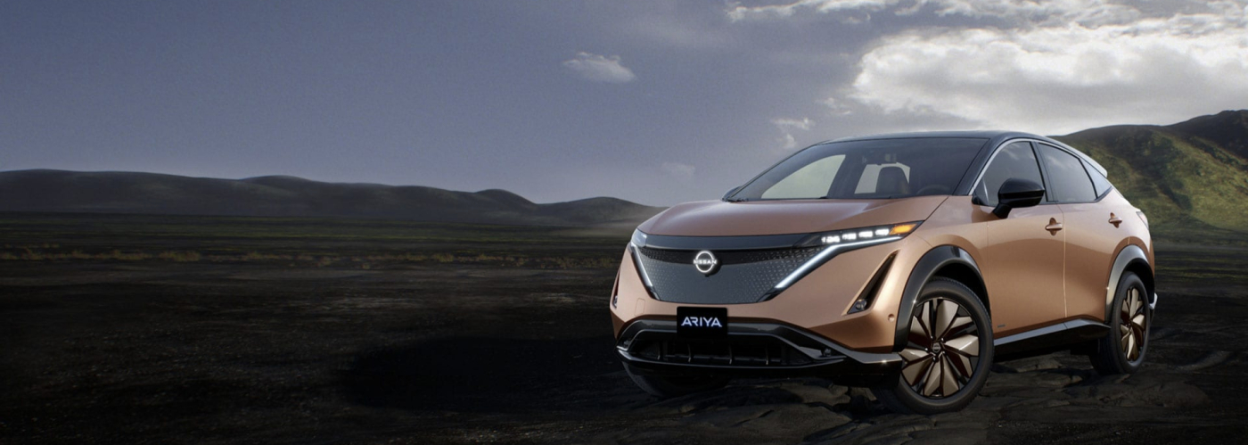 A gold Nissan Ariya is parked with mountains in the background.