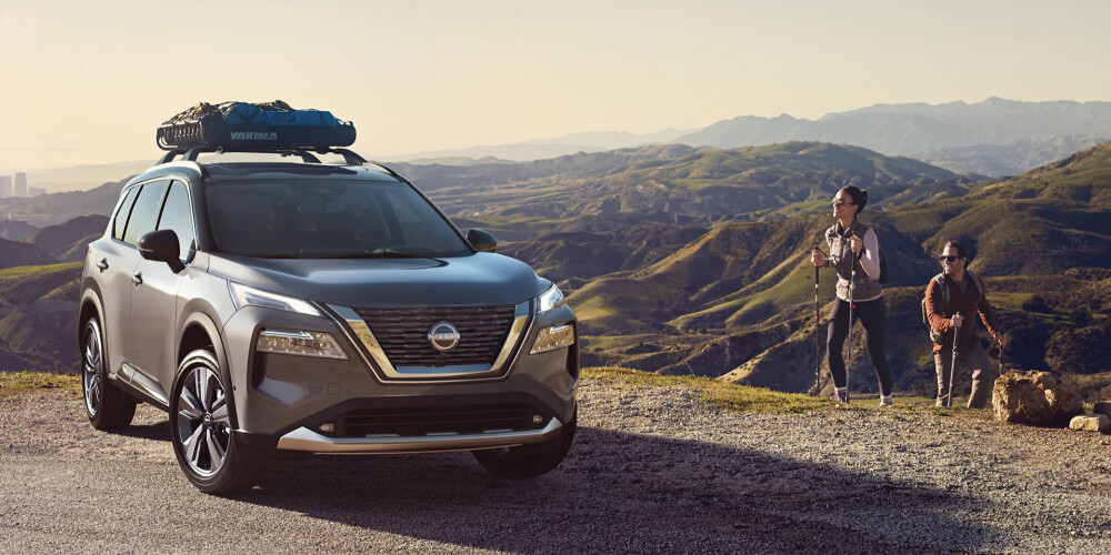 A couple hikes towards a grey 2023 Nissan Rogue parked upon a hill.