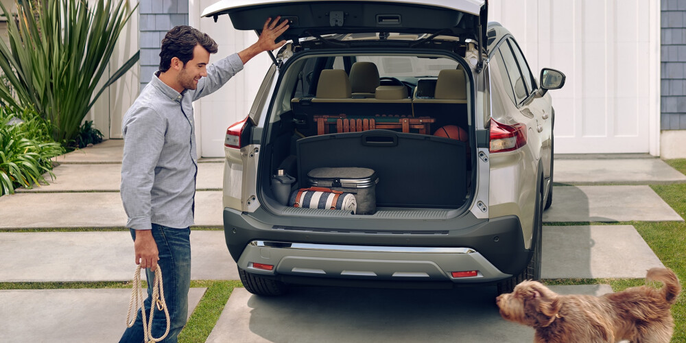 A man opens the trunk of a Nissan Rogue for his dog.