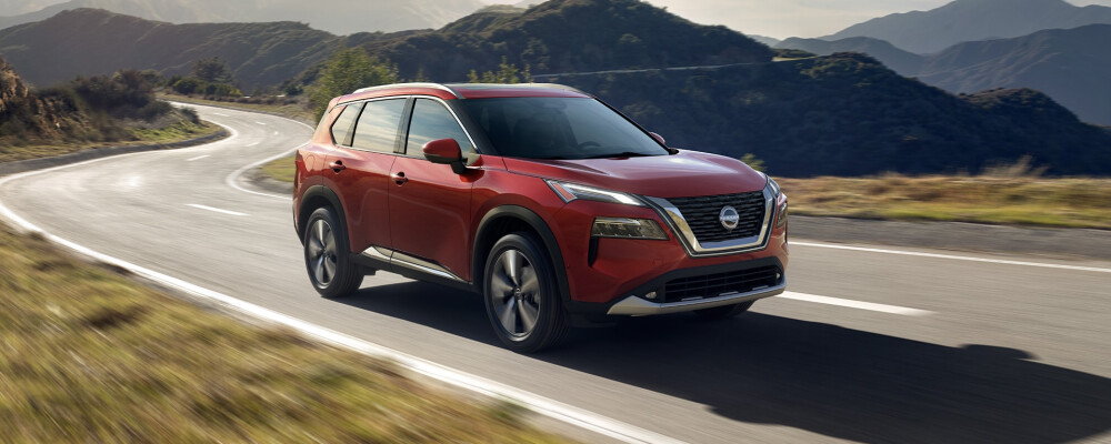 A red 2023 Nissan Rogue drives down a winding road in the mountains
