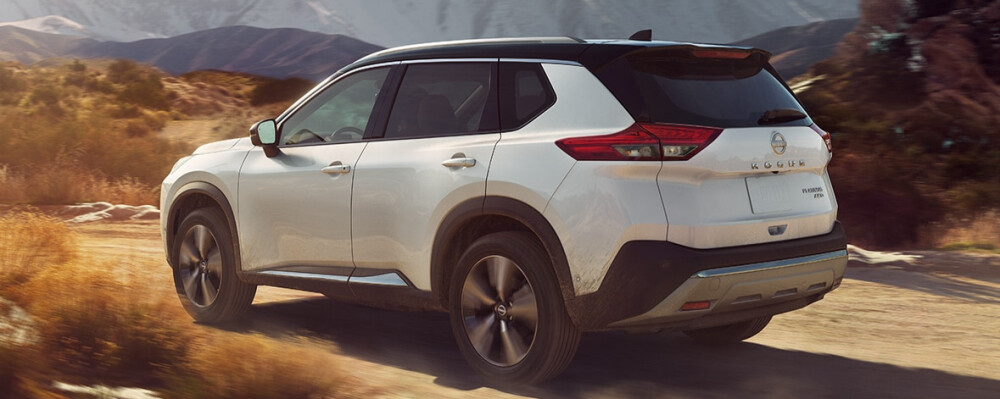 A white 2023 Nissan Rogue drives down a dirt road through the mountains.